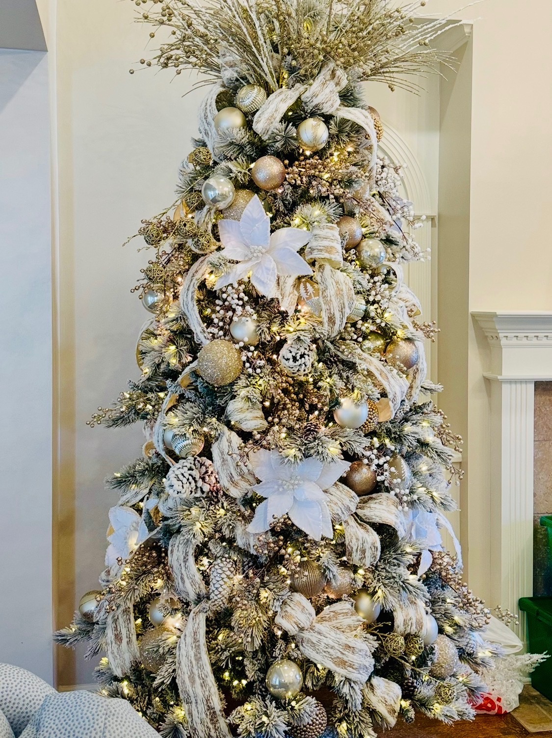 Flocked tree styled in ivory, gold and white poinsettias beside a fireplace
