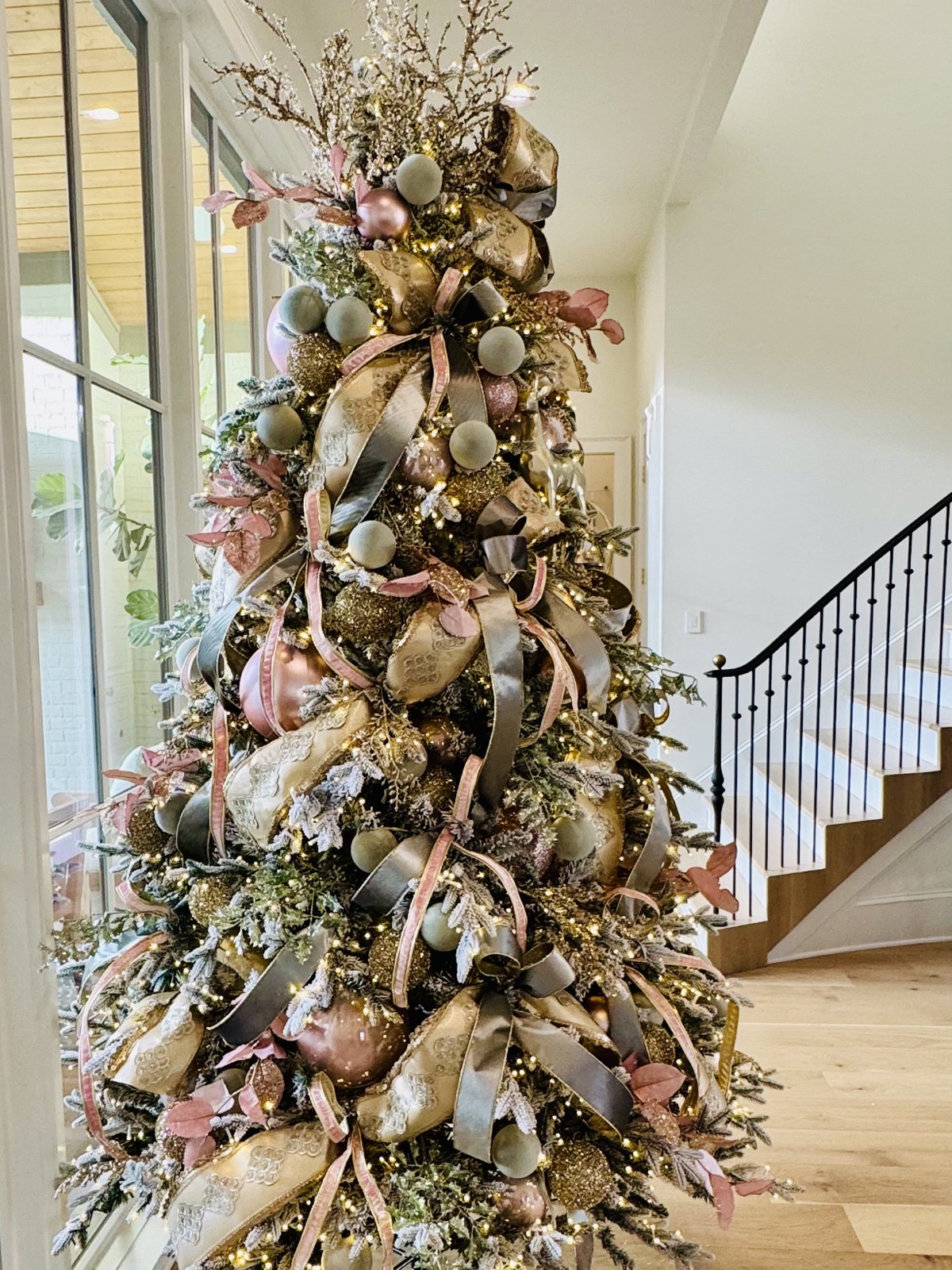 Flocked Christmas tree with champagne, blush and sage ribbon in an entryway